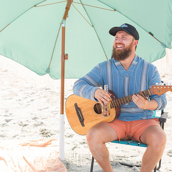 A man sitting on a beach chair while playing the guitar underneath an umbrella held up by the Suncoast Beach Shade umbrella anchor