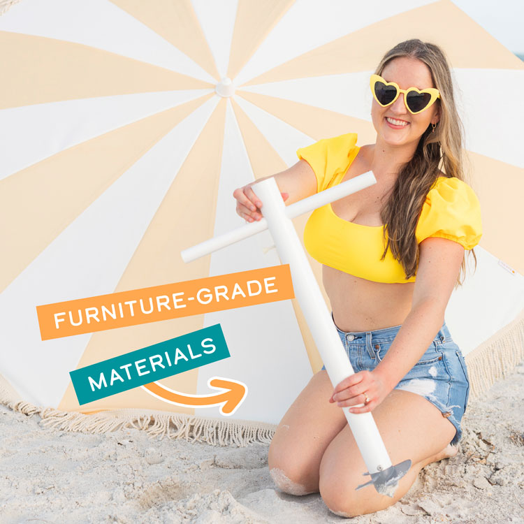 A woman smiling in front of an umbrella as the background as she holds the Suncoast Beach Shade umbrella anchor in front of her with the words "Furniture-Grade Materials" on top of the image